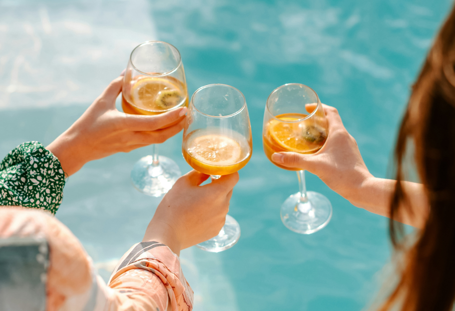 a group of hands holding wine glasses with orange liquid in the air