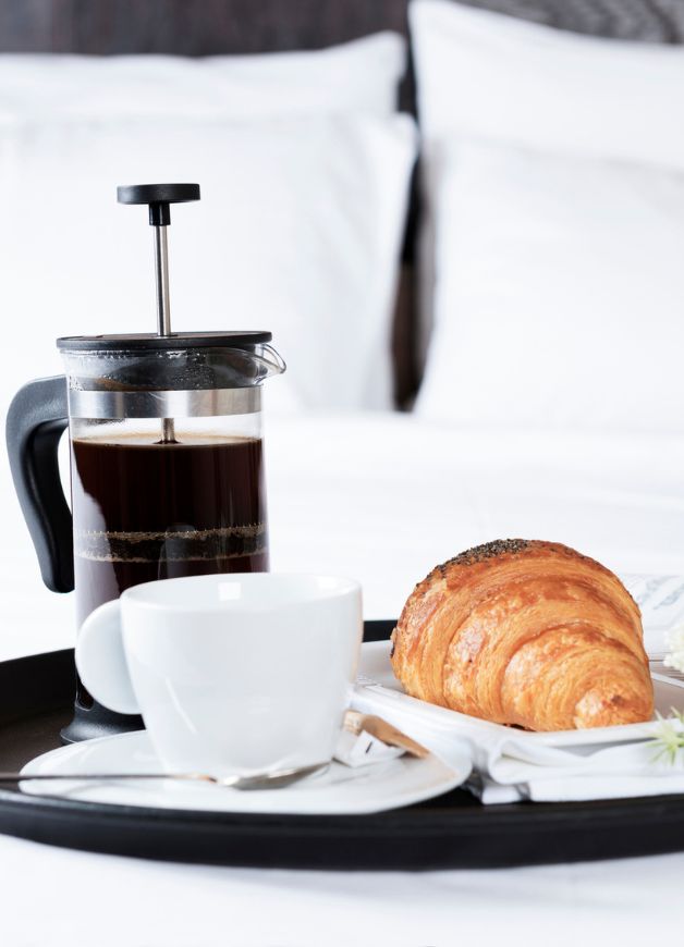 a breakfast tray with a coffee maker and croissant