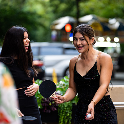 two women in black dresses holding ping pong paddles and smiling