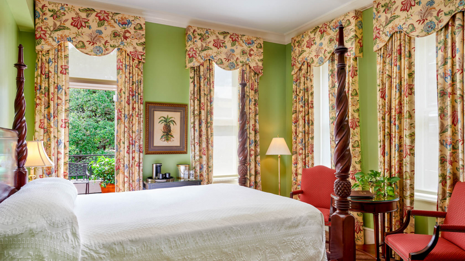 A wide view of a bedroom with a four-poster bed, floral curtains, and green walls.