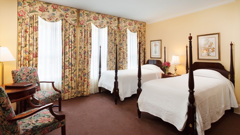 A hotel room with two beds, floral curtains, and comfortable seating.
