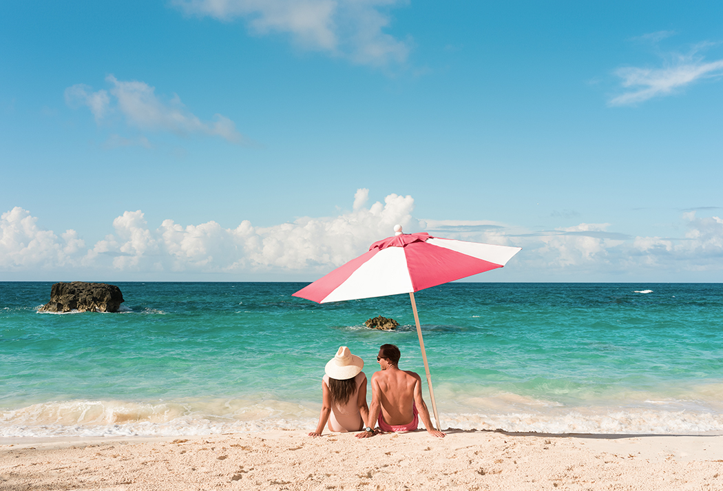 a man and woman sitting on a beach under an umbrella