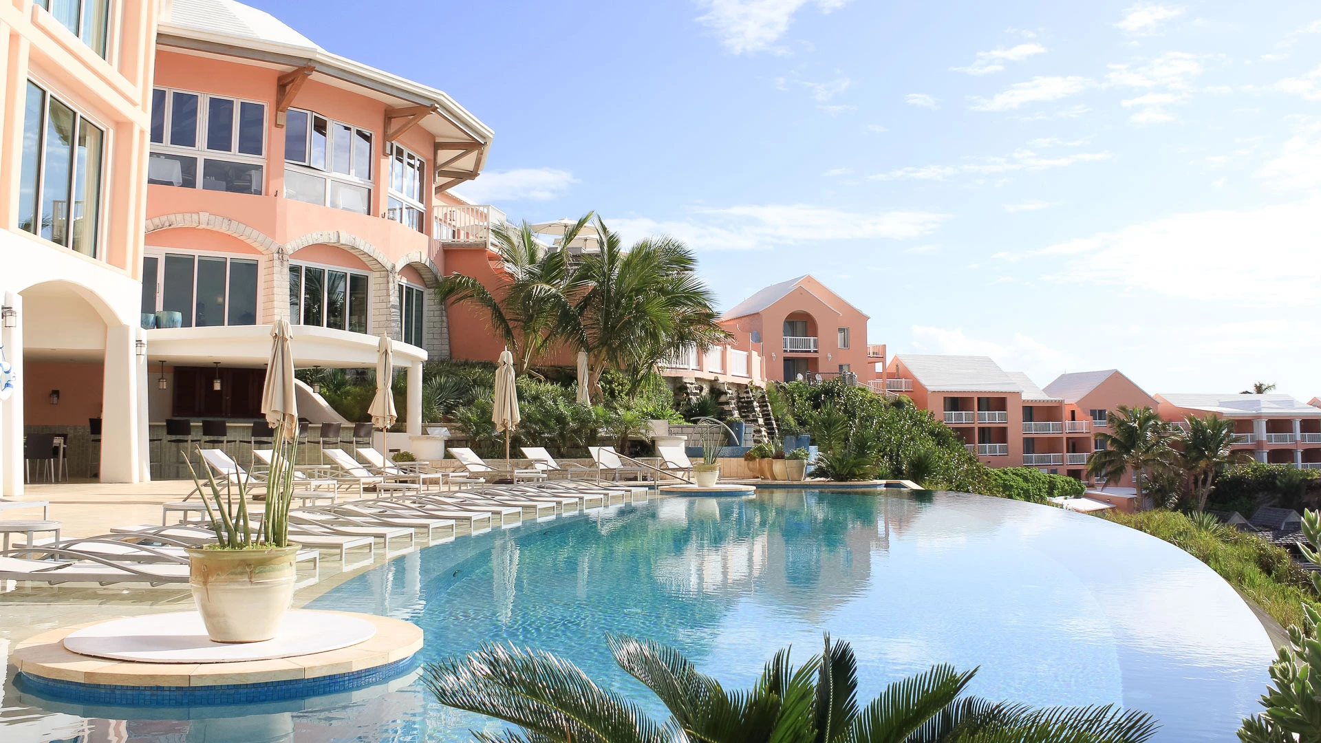 a pool with lounge chairs and palm trees in front of a building
