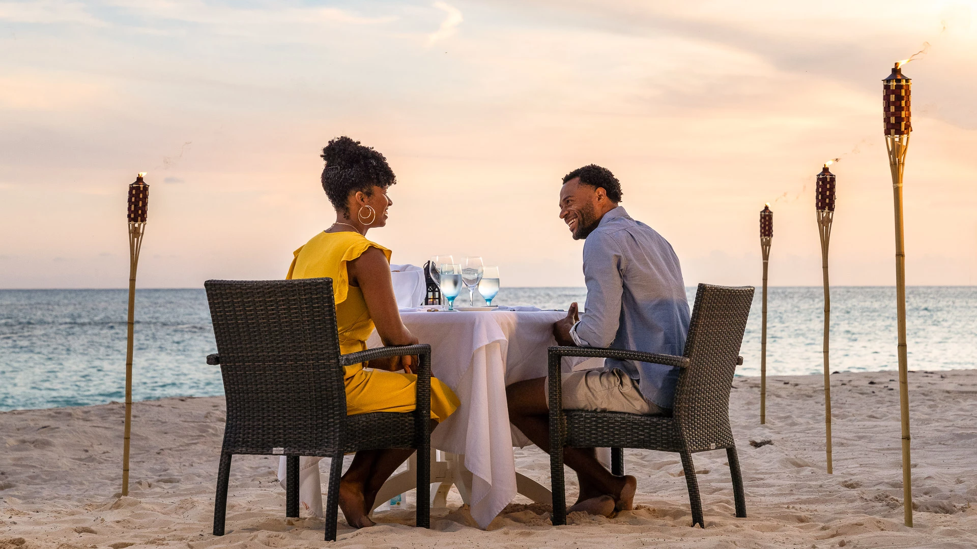 a man and woman sitting at a table on a beach