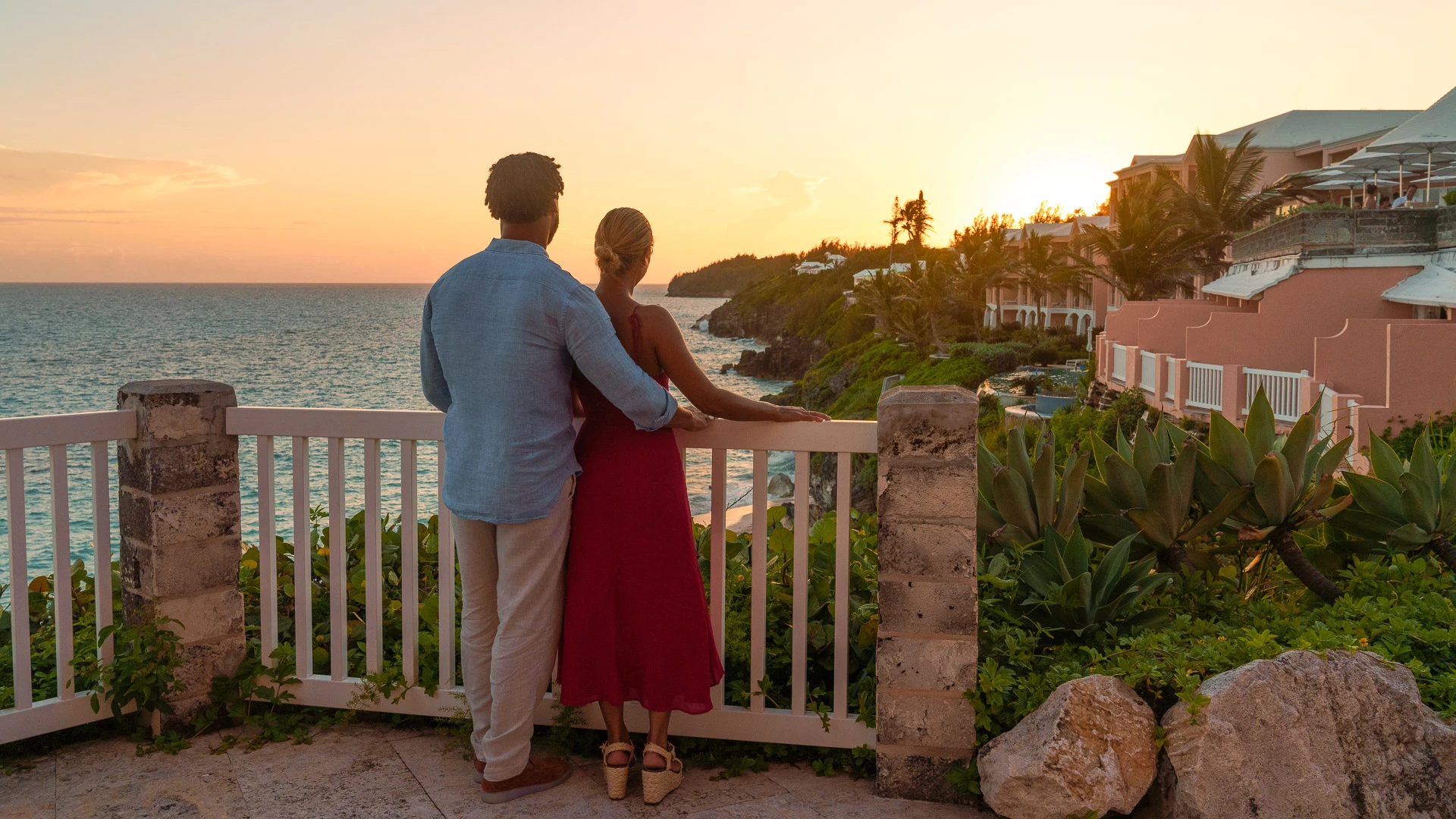 a man and woman standing on a balcony overlooking a body of water