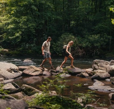 a man and woman walking on rocks in a river