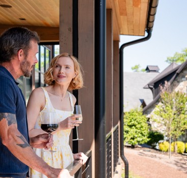 a man and woman standing on a porch with wine glasses