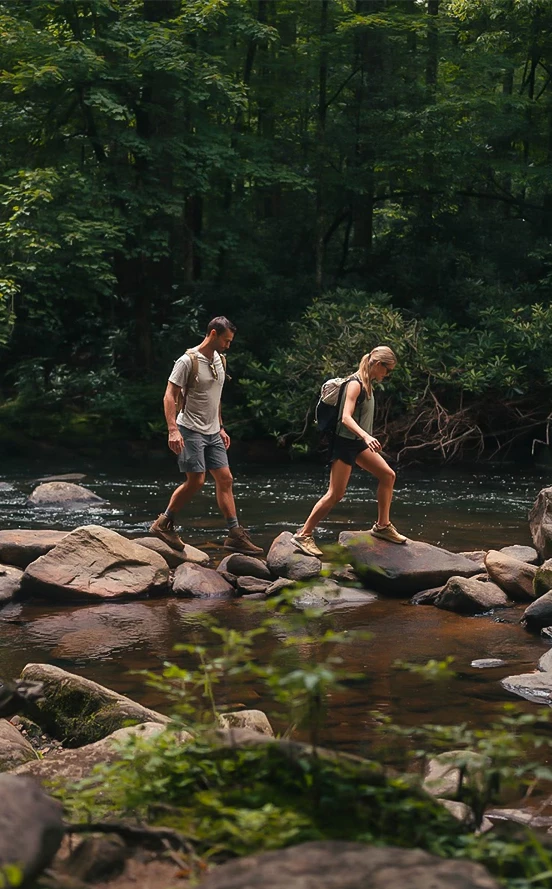a man and woman walking on rocks in a river