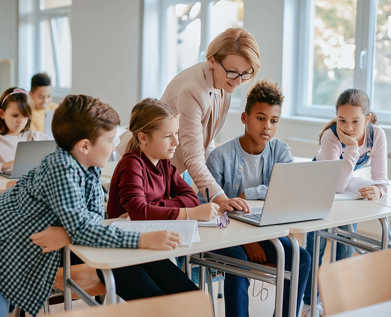 a group of kids sitting at desks with a laptop