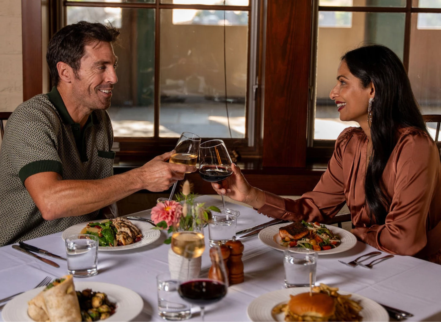 a man and woman sitting at a table with food and drinks
