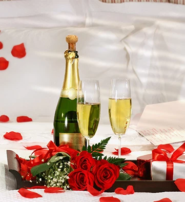 a bottle and glass of champagne on a bed with roses