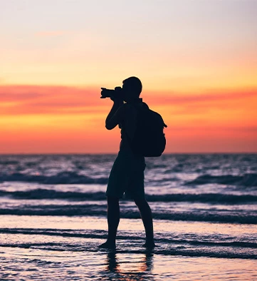 a man taking photos on the beach during sunset
