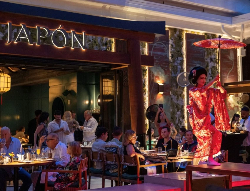 A dining area with people sitting at tables and a performer in a red kimono on a table.