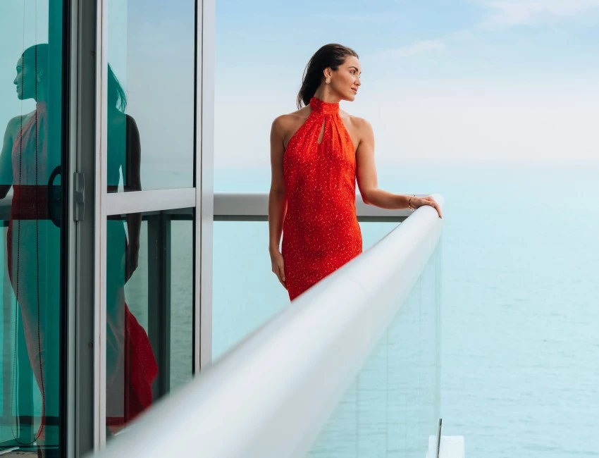 a woman in a red dress standing on a balcony overlooking the ocean