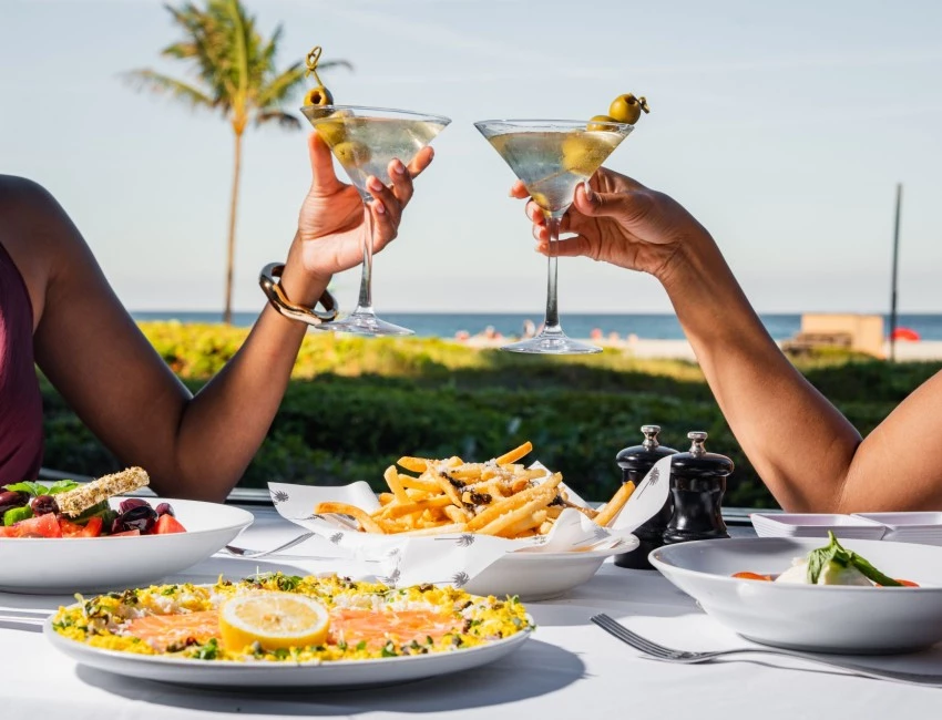 a couple of people holding drinks and sitting at a table with food