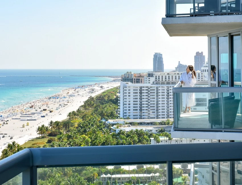 a woman wearing a white robe looking at the ocean from her balcony