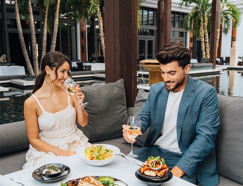 a couple enjoying food and drinks outdoor with palm trees behind them