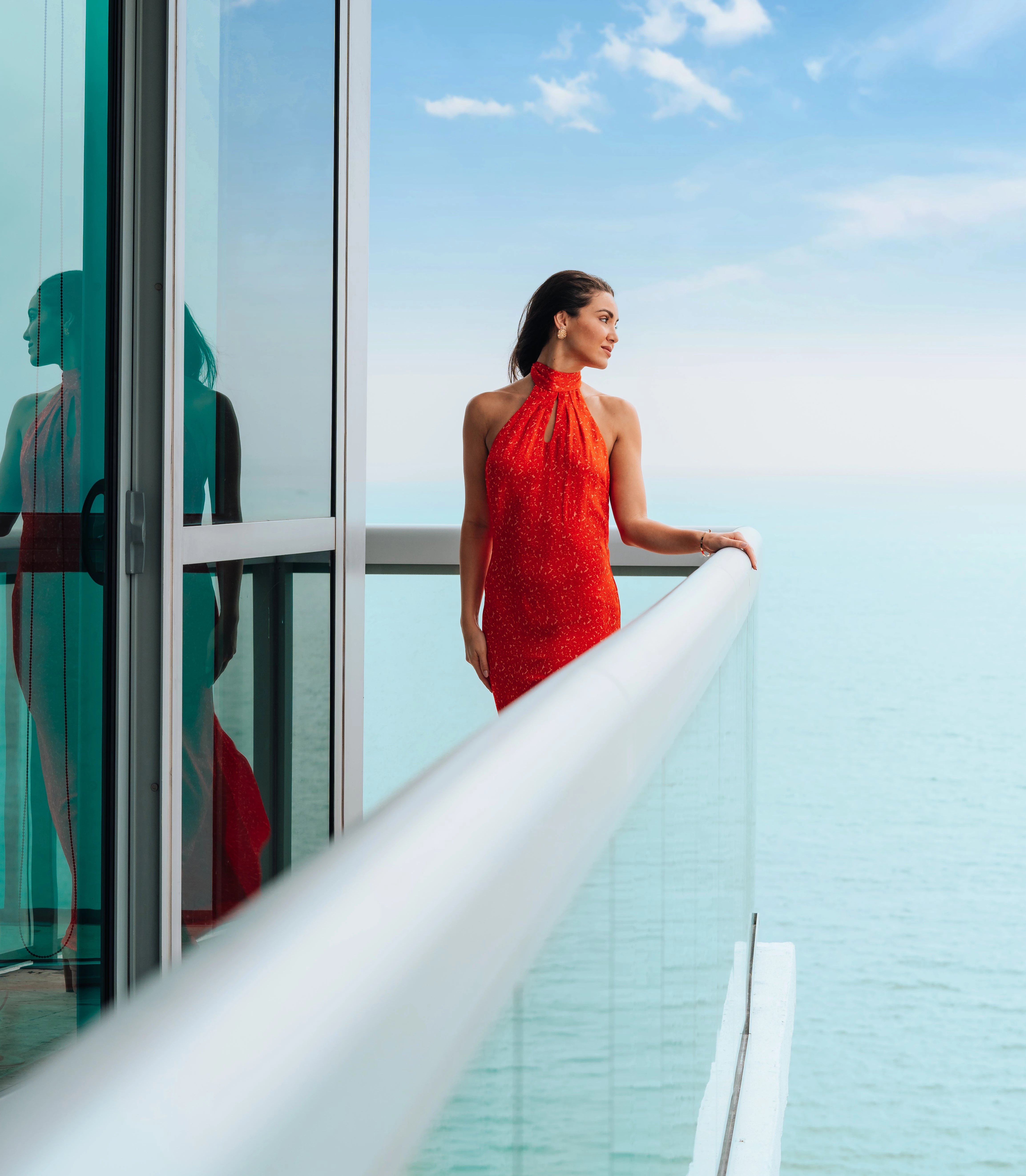a woman in a red dress standing on a balcony overlooking the ocean