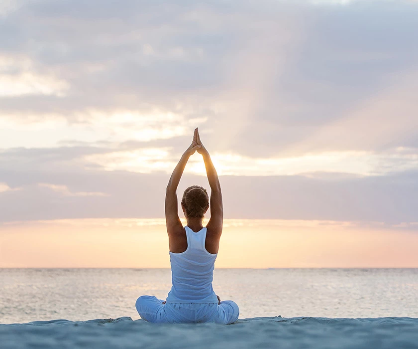 a woman sitting on the beach doing a yoga pose at sunrise