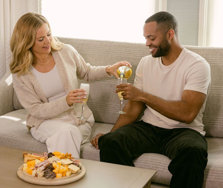 a man and woman sitting on a couch and drinking wine