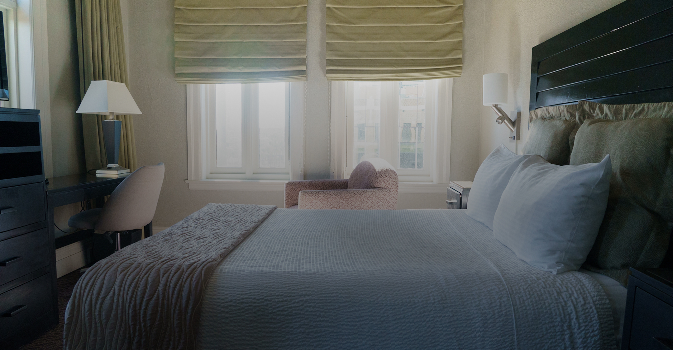 a bed with pillows and a chair in a room with windows