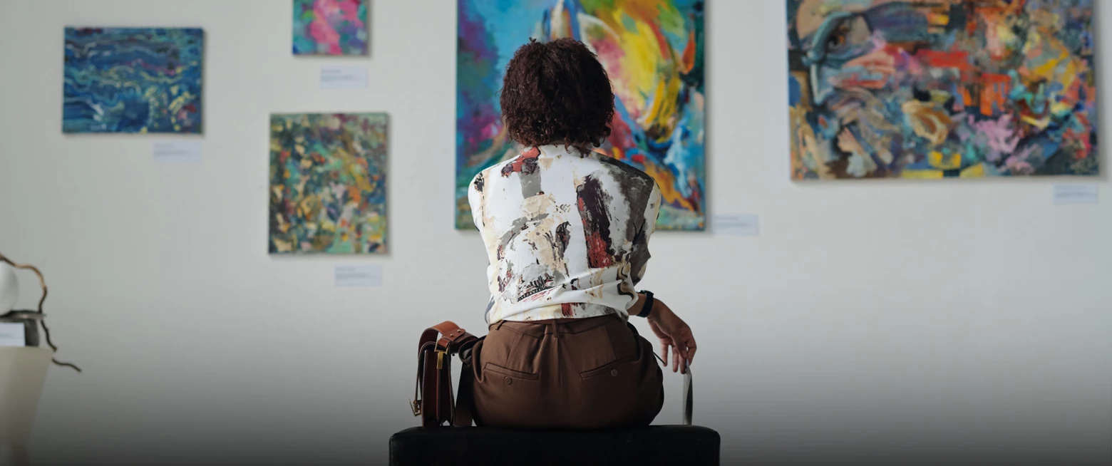 a person sitting on a suitcase looking at paintings