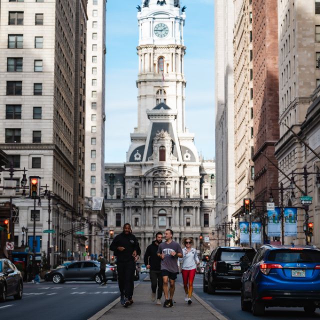 a group of people walking on a street with cars and a clock tower