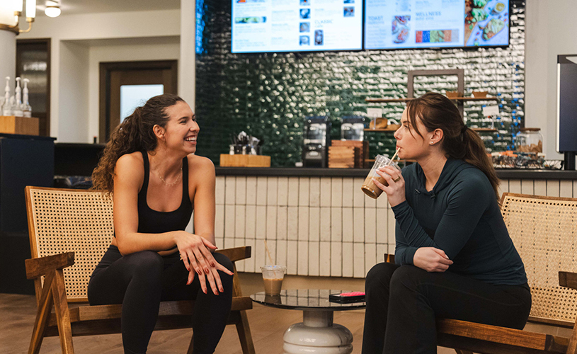 two women sitting in chairs and drinking from a straw