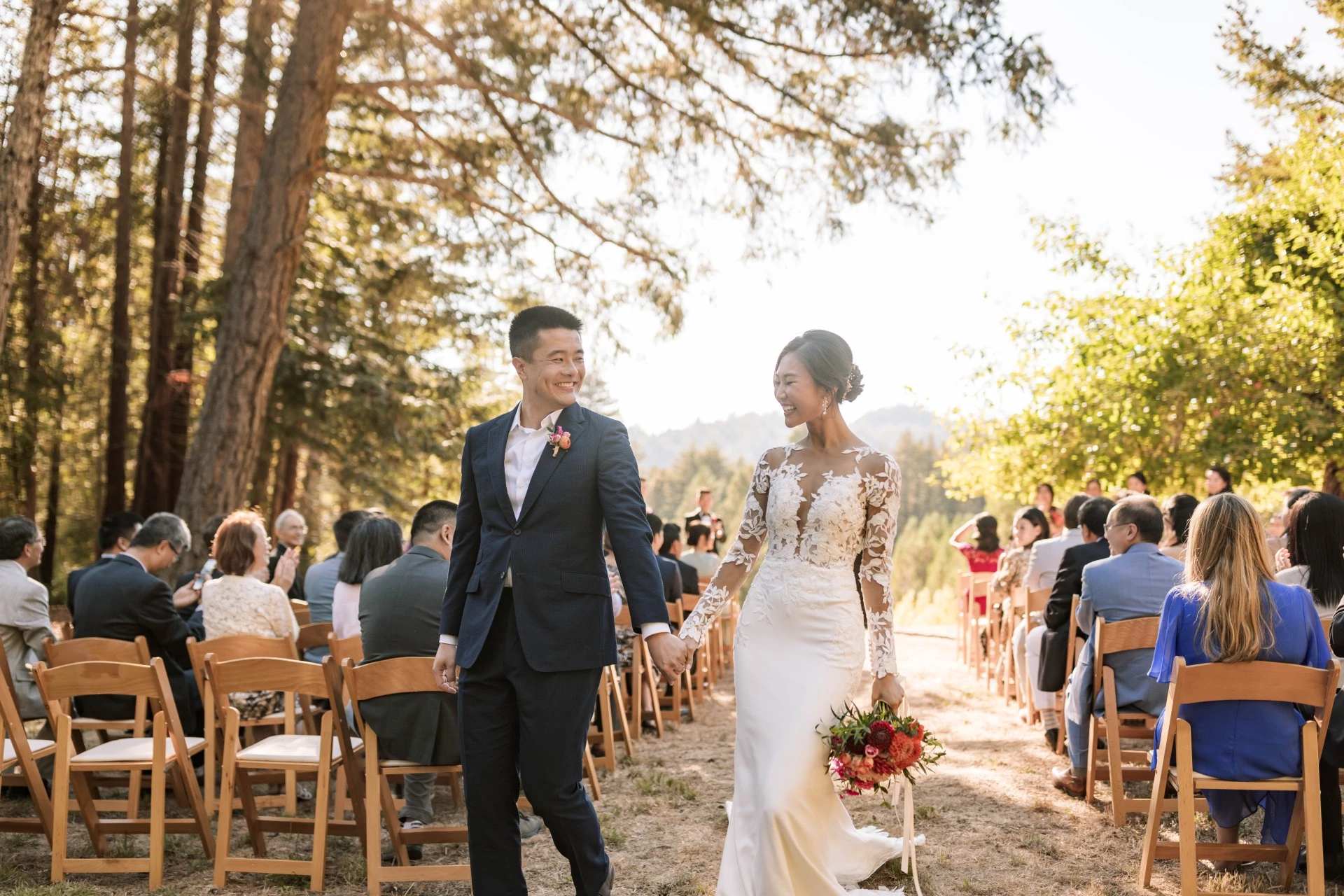 a man and woman holding hands and walking down a path with chairs and trees