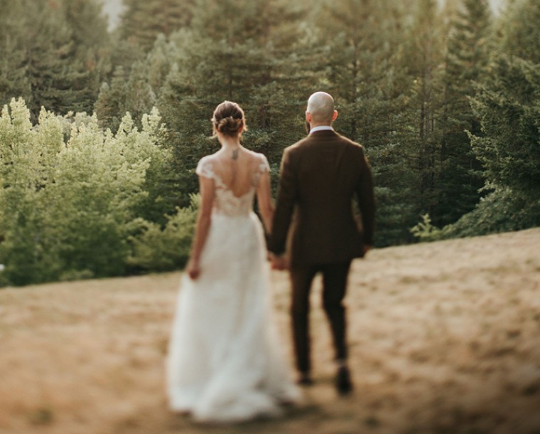 bride and groom dressed up walking through field over looking at trees