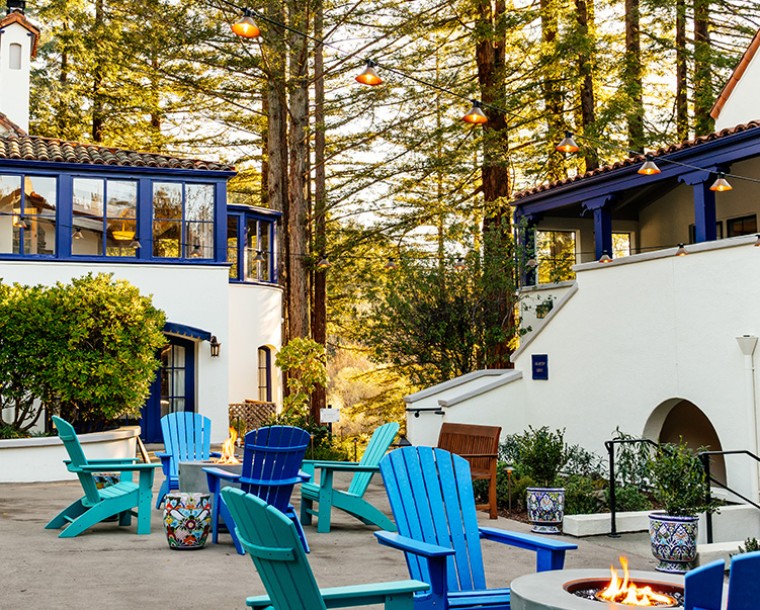 courtyard with different shades of blue chairs around fireplace and tall trees in back