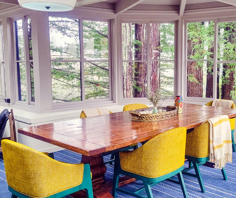 stavrand Sun Room with yellow and teal chairs around table overlooking windows to forest