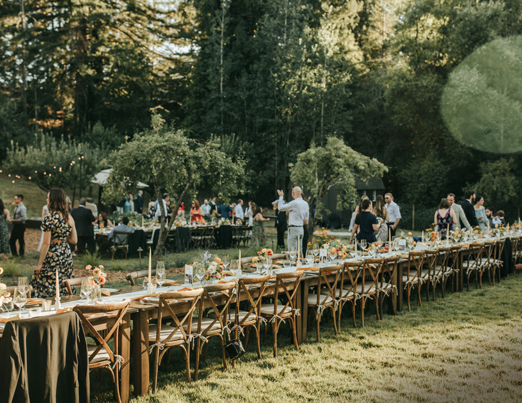 wedding reception set up with long table decorated with flowers and plates, guest mingling in the back