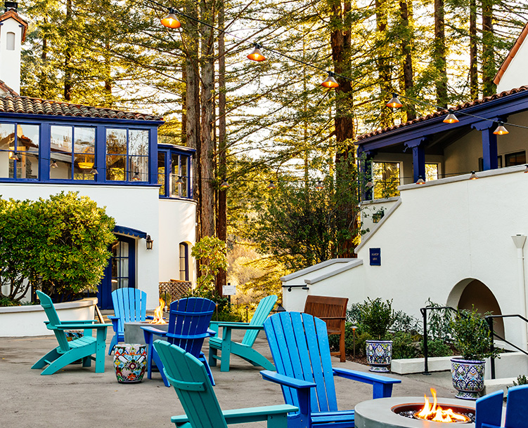 courtyard with different shades of blue chairs around fireplace and tall trees in back
