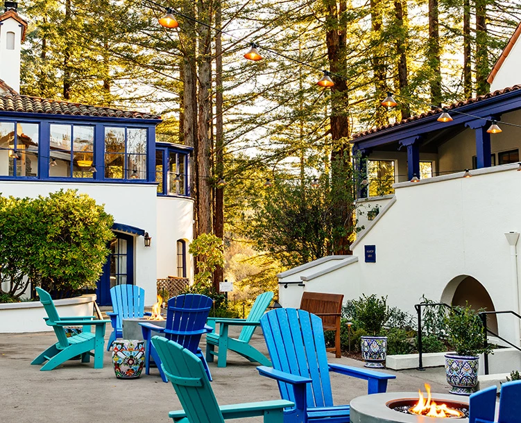 courtyard with different shades of blue chairs around fireplace and tall trees in back