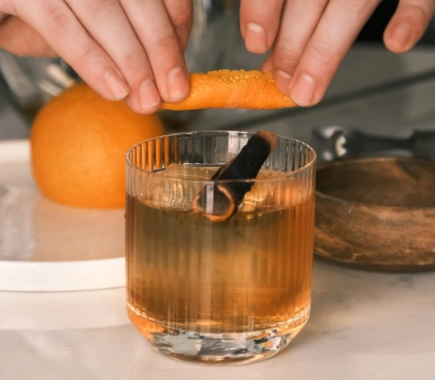 a person holding an orange peel over a glass of liquid