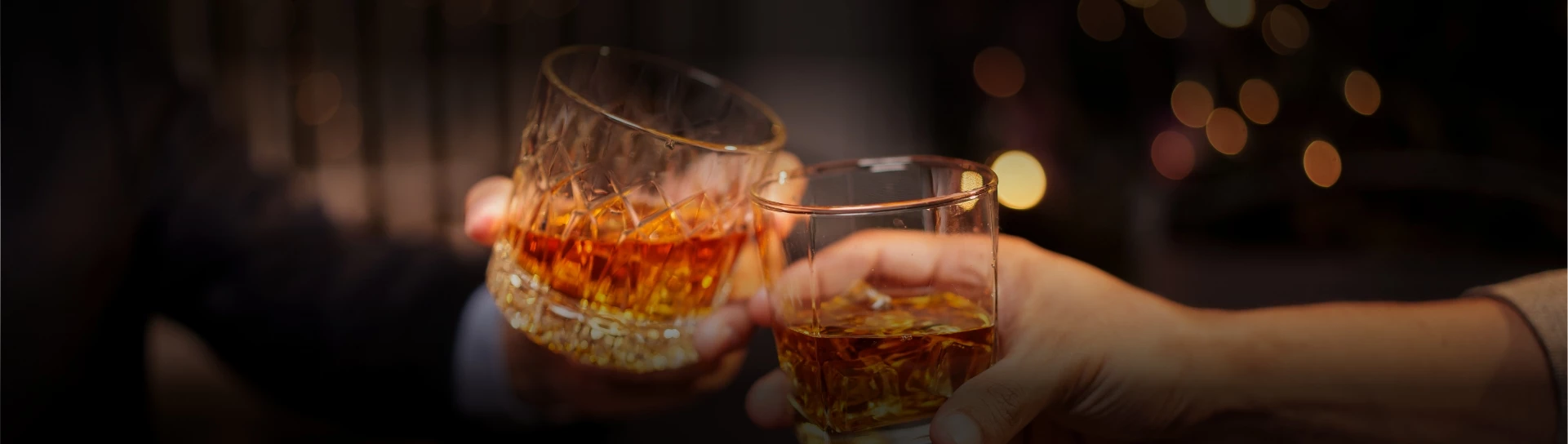 a pair of hands holding glasses with amber liquid