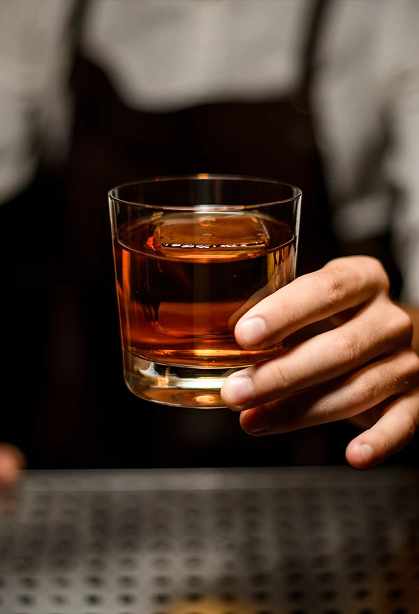 a hand holding a glass of amber liquid