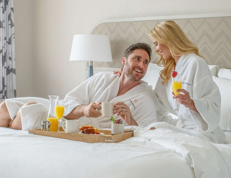 a man and woman in white robes in bed with breakfast tray