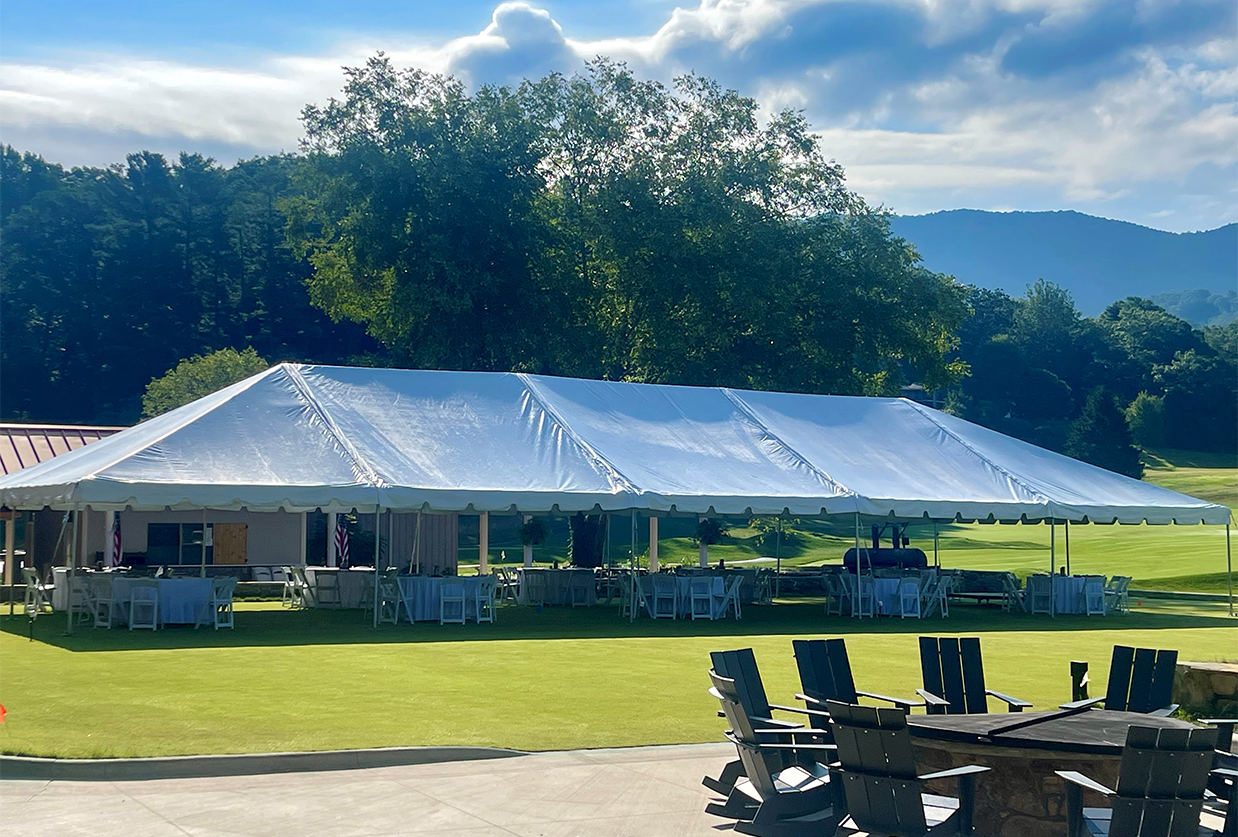 a white tent with chairs and tables in front of a lawn