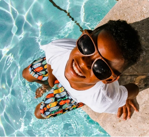 a boy wearing sunglasses and standing on a ledge of a pool