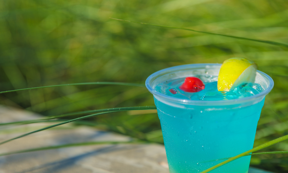 a blue drink with a cherry and a slice of lemon in a plastic cup