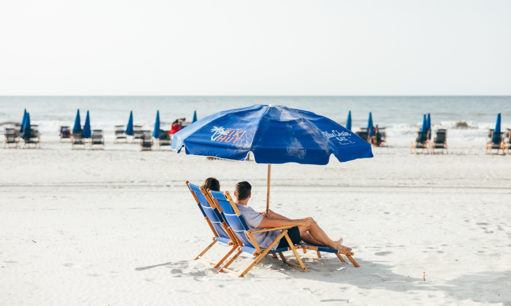 a man and woman sitting under a blue umbrella on a beach