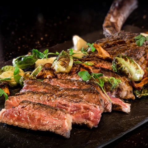 a large steak with vegetables on a black plate