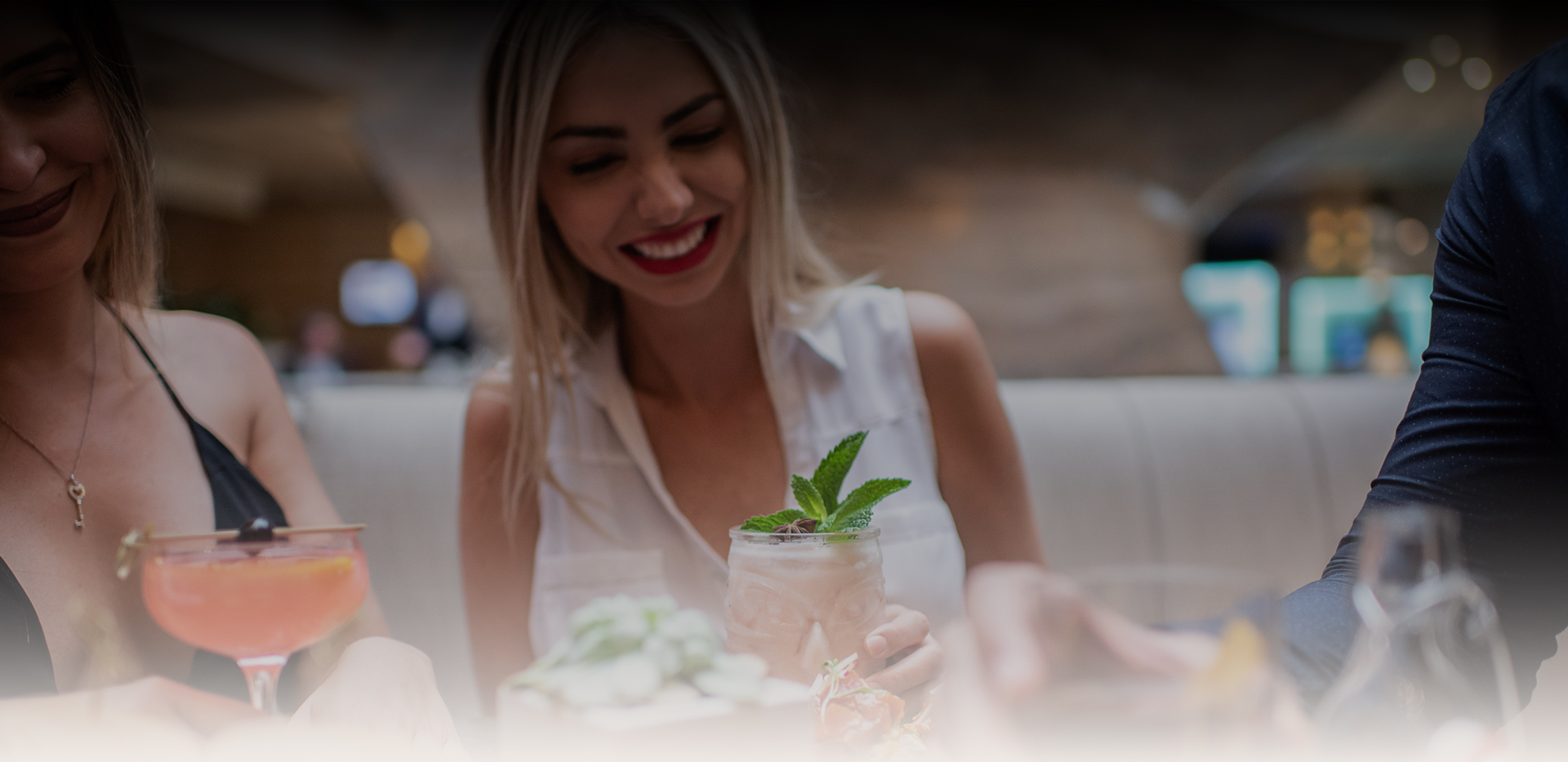a woman smiling at a table with a drink