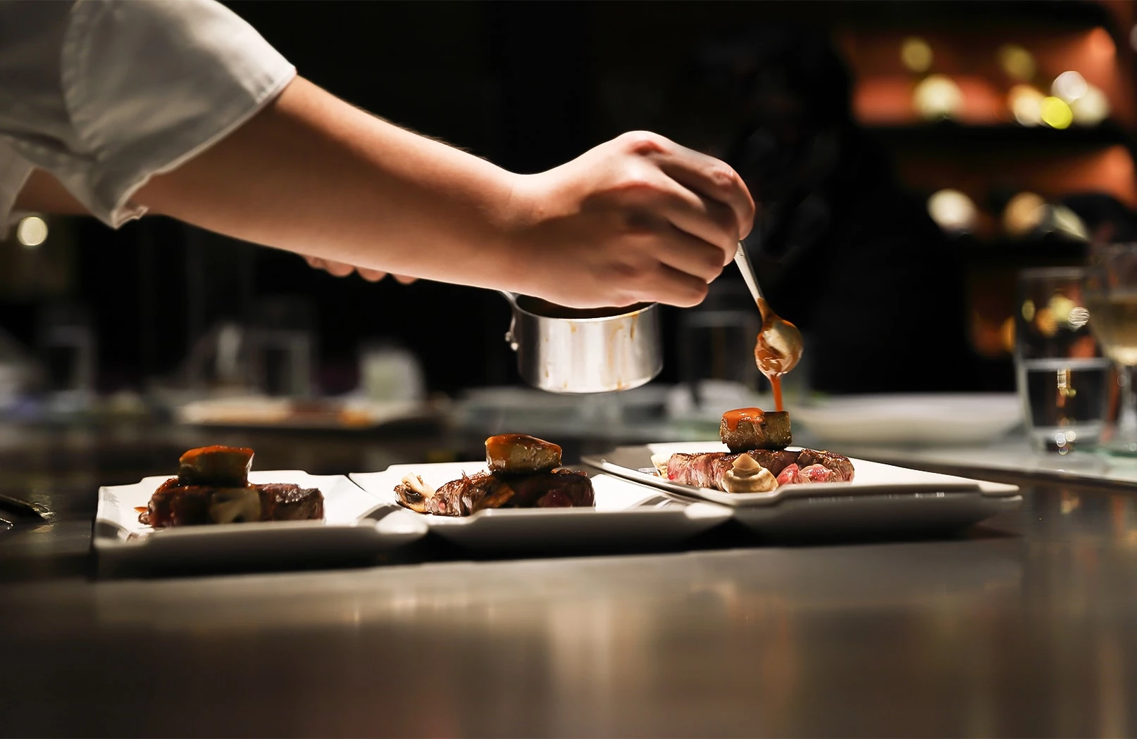 a chef providing last touches on three dishes in kitchen
