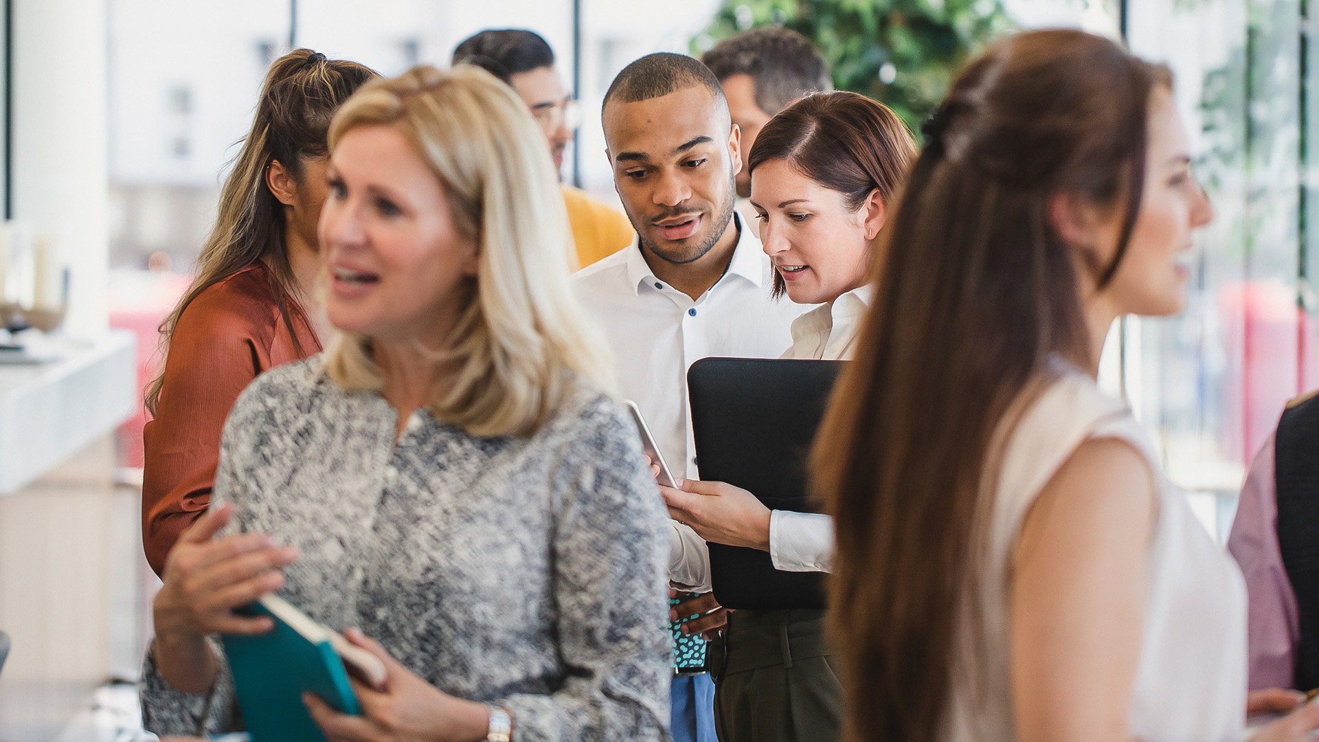 group of diverse professionals mingling in a bright corporate setting while reviewing documents and digital devices