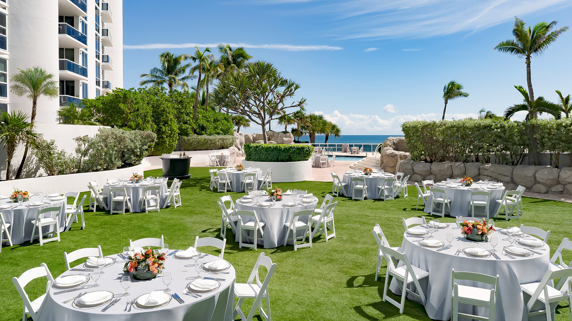 a group of tables and chairs in a grassy area with a pool and trees