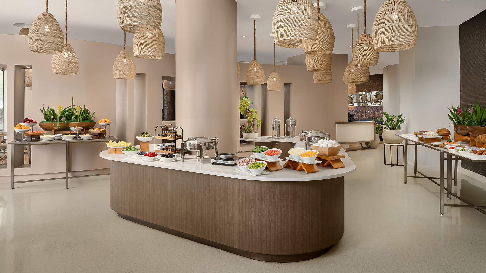 spacious hotel buffet dining area with woven pendant light fixtures hanging above curved food stations and fresh produce displays