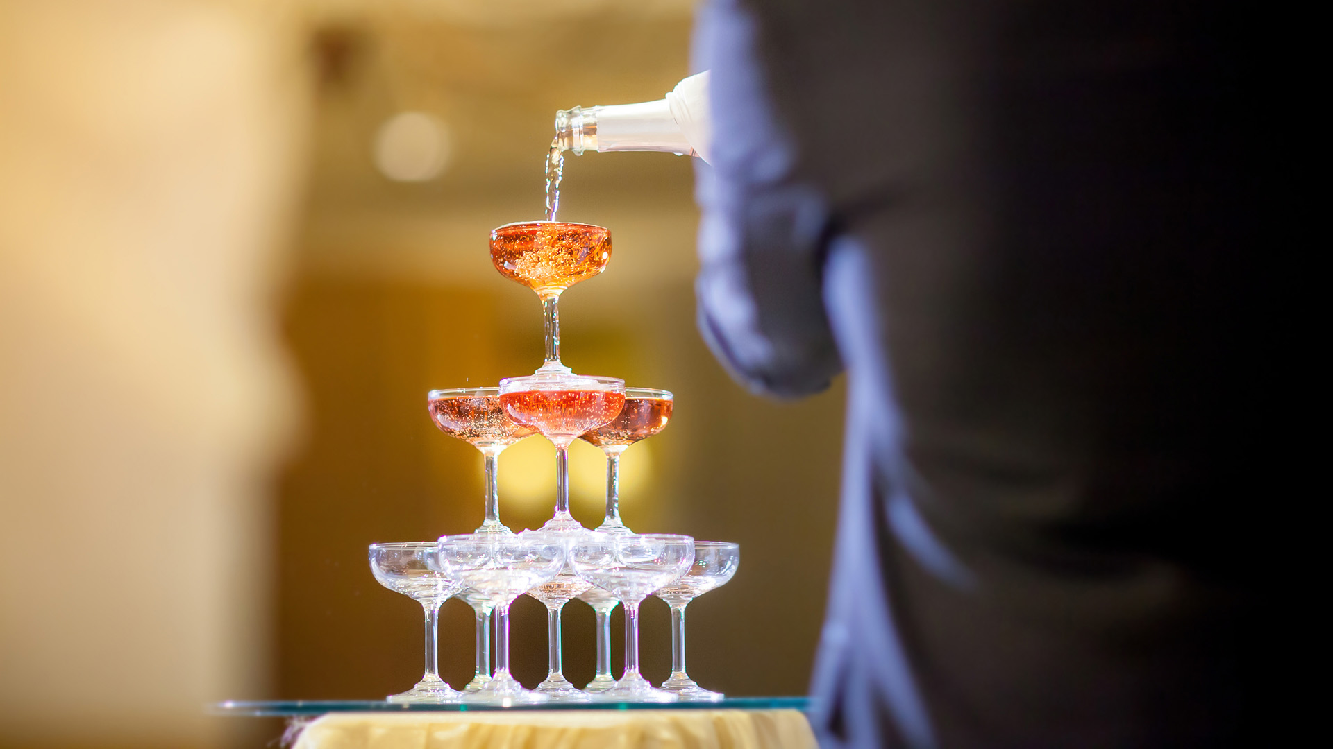 a person pouring liquid into a pyramid of champagne glasses
